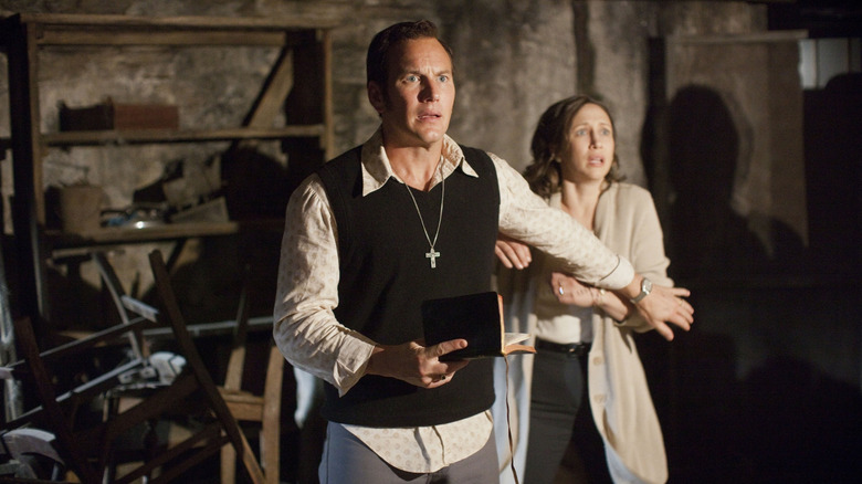 Patrick Wilson as Ed Warren with a bible in his hand with Vera Farmiga as Lorriane Warren standing behind him in The Conjuring