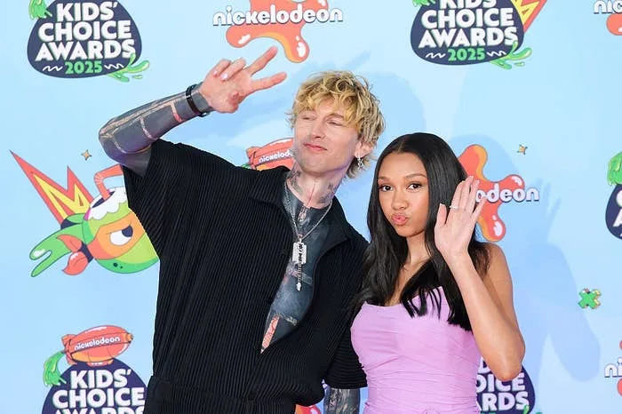 Two celebrities pose stylishly at the 2025 Kids' Choice Awards, with one flashing a peace sign and the other in a chic dress