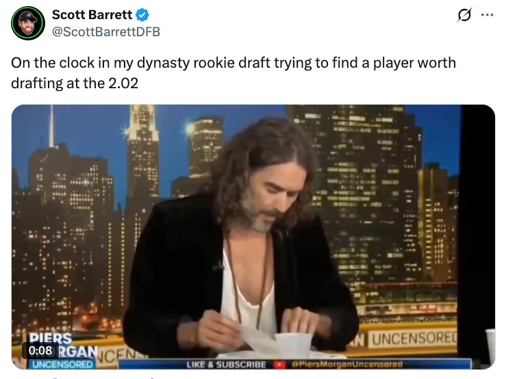 A person with long hair and a partially open shirt reads notes on a TV set with a cityscape backdrop. Tweet mentions a dynasty rookie draft