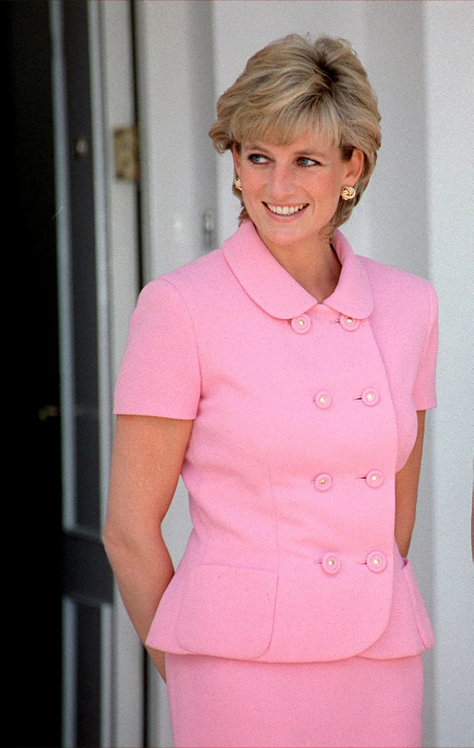 A woman in an elegant double-breasted suit with statement earrings stands smiling, looking to the side