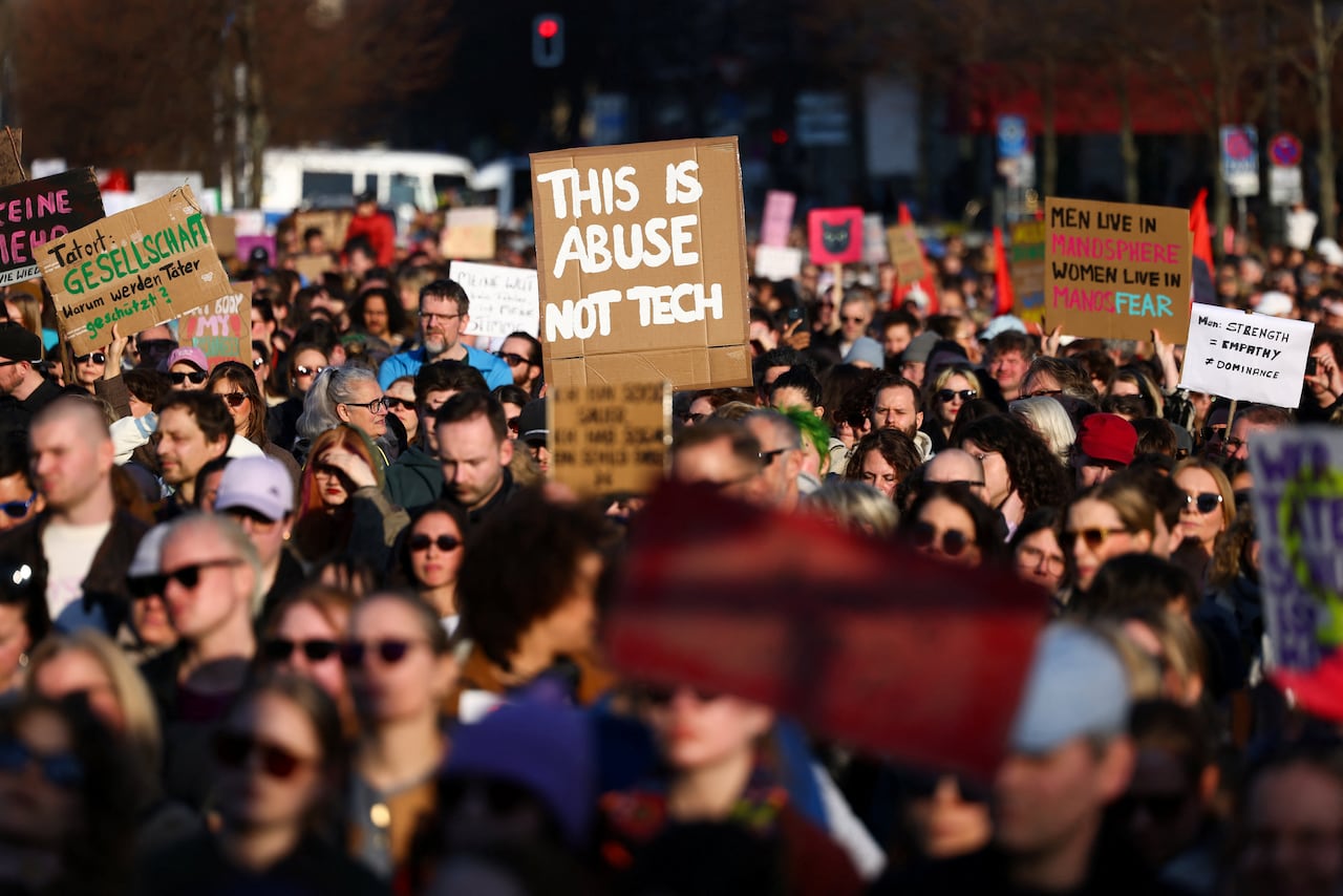 A crowd of protestors seen in the image, men and women, holding signs decrying violence against women online. 