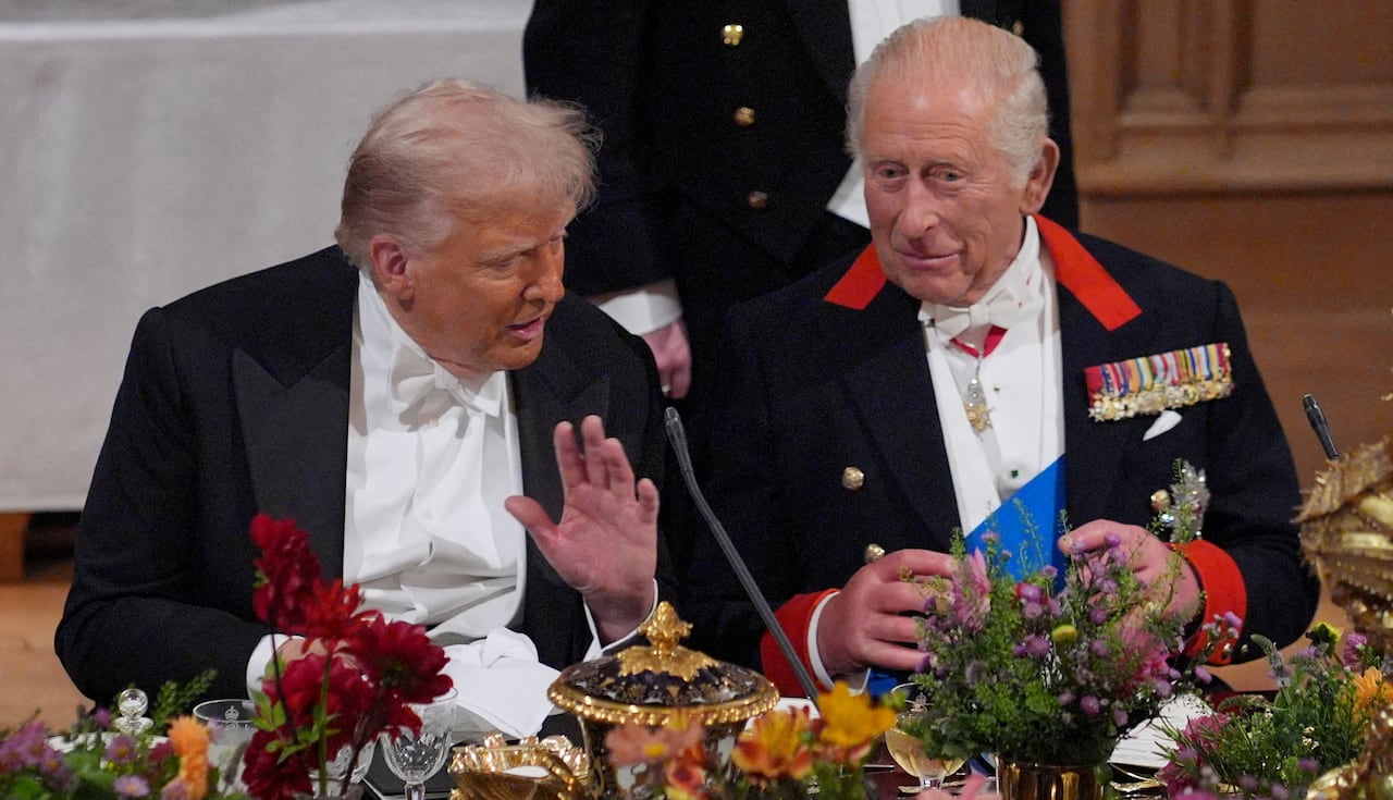 Two people talk while seated at an elaborately set dining table.