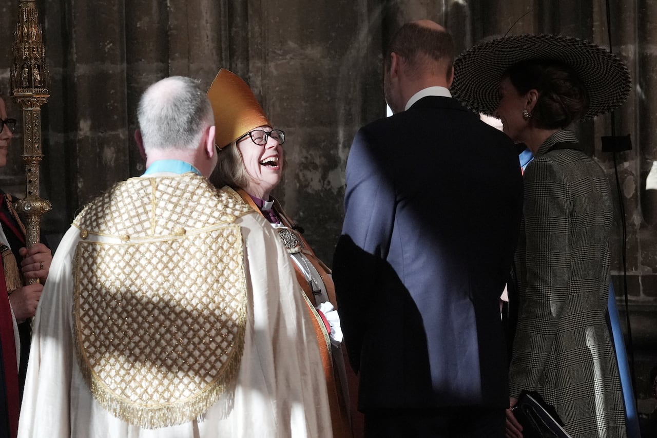 A person wearing religious vestments laughs as they talk with three other people in a stone cathedral.