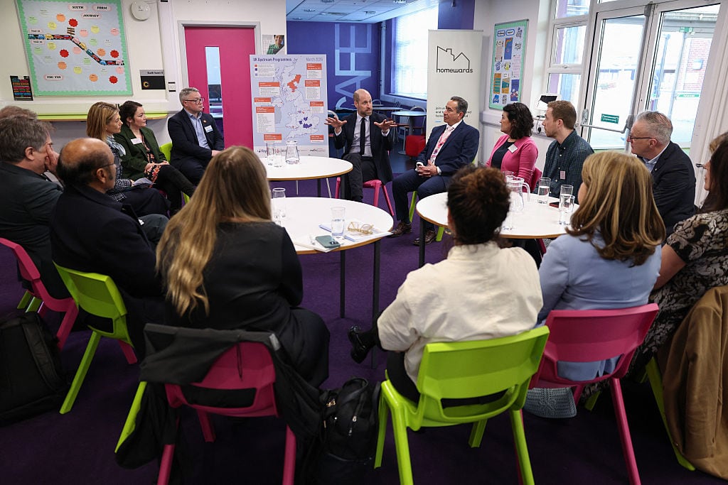 People sit on chairs in a circle with round tables in front of them.