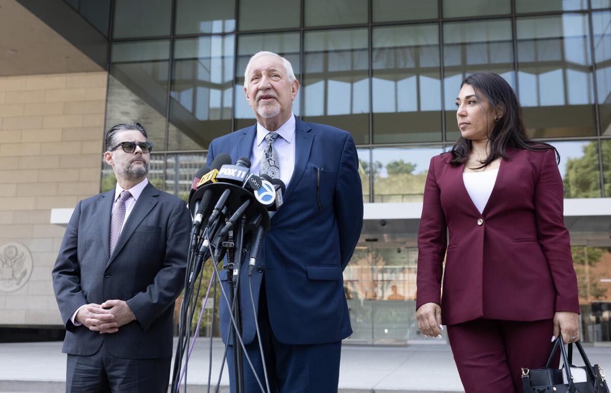 Three people in suits talk in front of microphones.