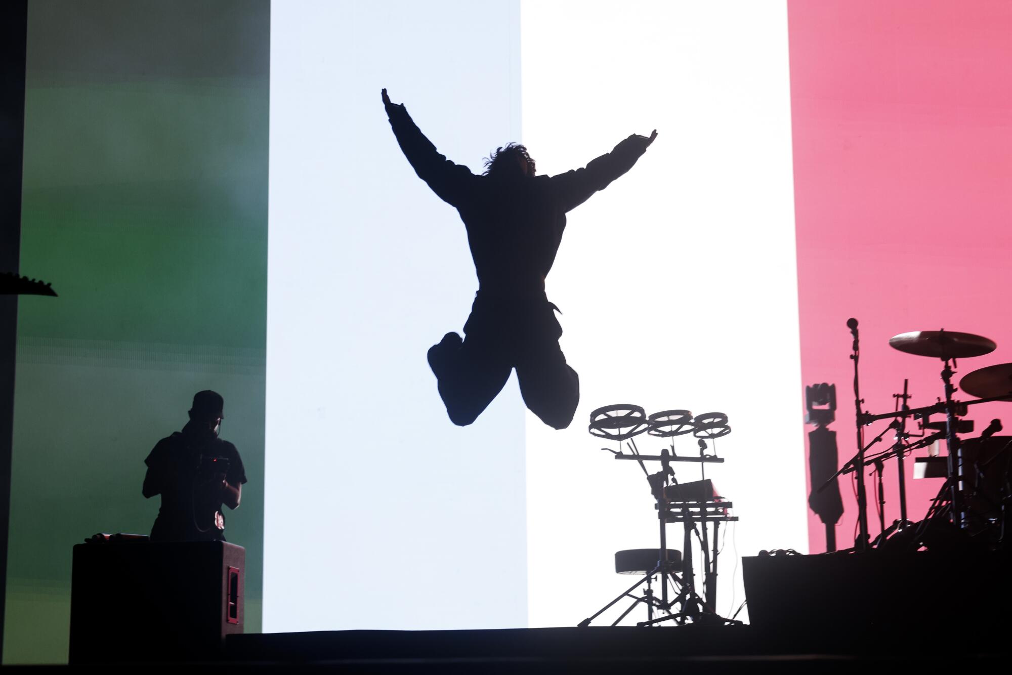 A silhouette of a person jumping in the air on a stage near equipment
