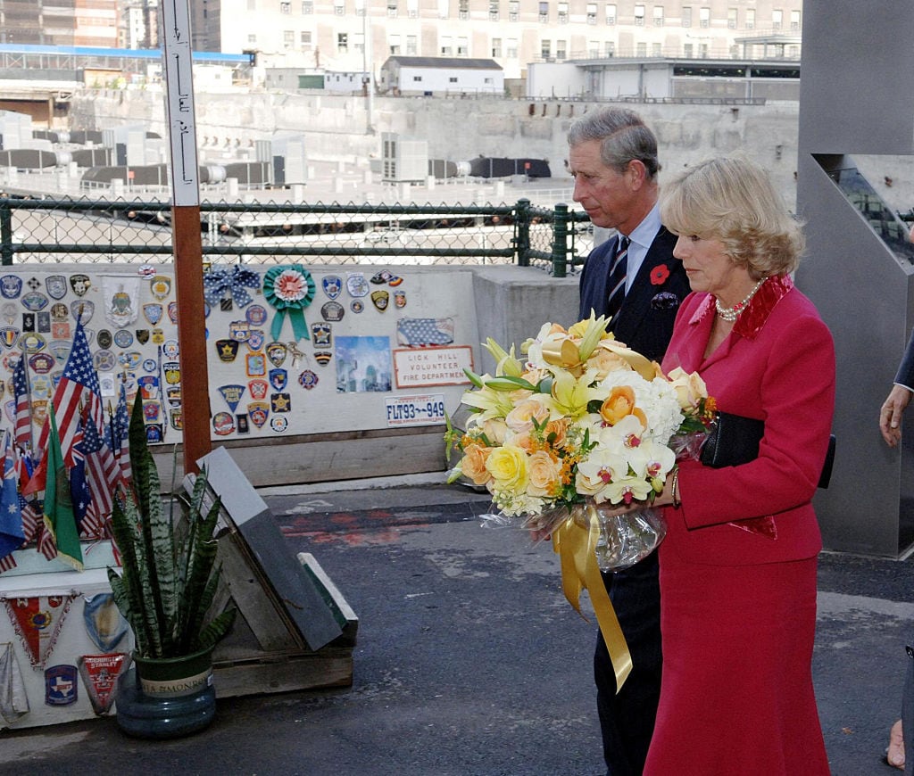 Two people, one holding flowers, stand at a memorial.