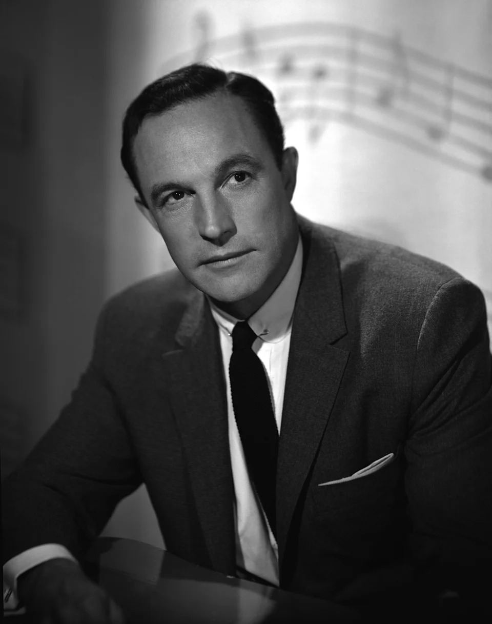 Gene Kelly in a suit poses thoughtfully against a backdrop with musical notes