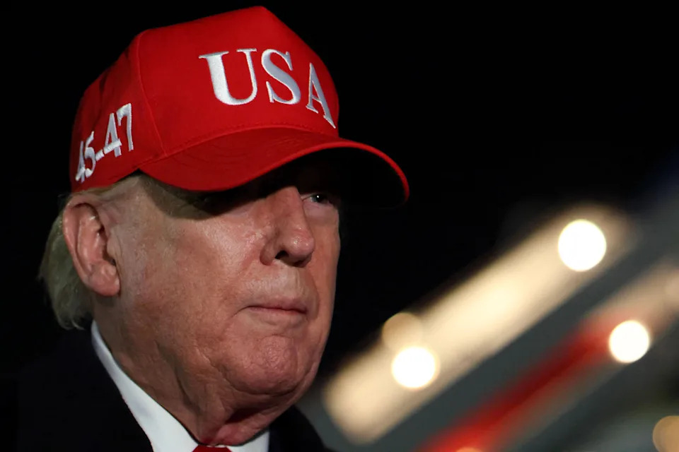 Donald Trump wearing a "USA" cap with aircraft steps in the background