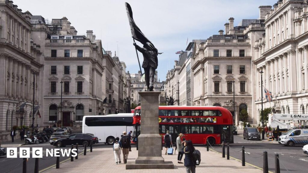 A grey statue of a man wearing a suit, marching forward, carrying a flag that covers his face