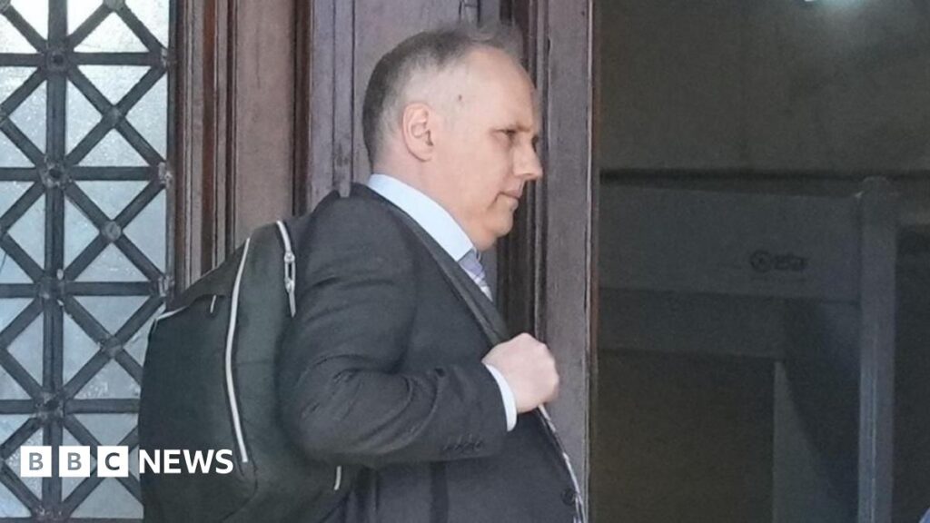 Ex-BBC producer guilty of possessing or making indecent images of children Dylan Dawes standing leaning on a door. He has a bag over his shoulder.