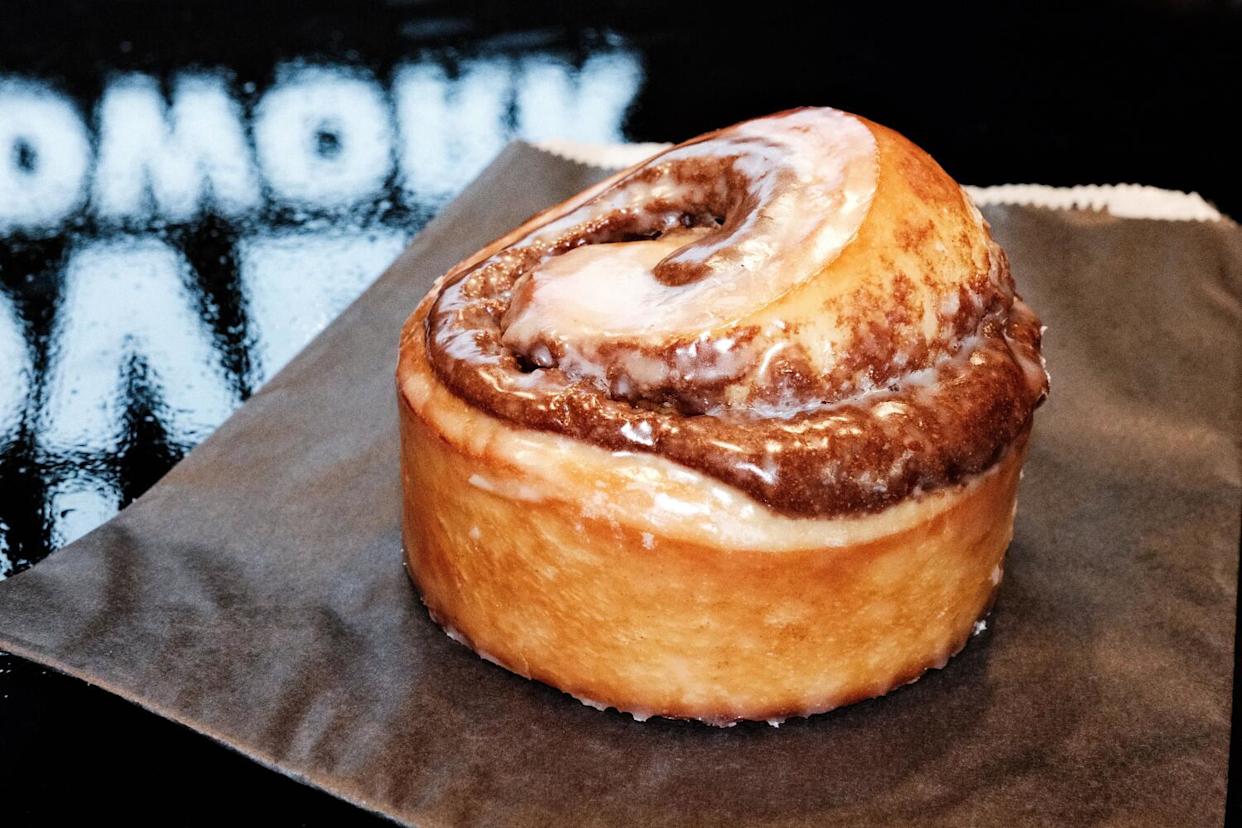 A doughnut-glaze cinnamon bun atop black paper atop a reflective black table