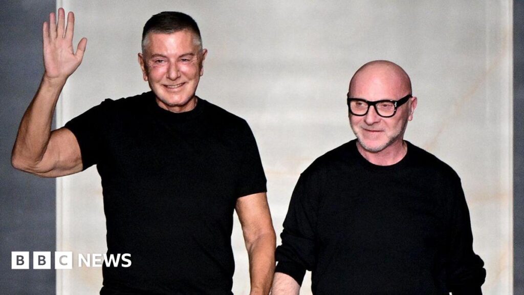 Domenico Dolce and Stefano Gabbana salute the audience at the end of the Dolce & Gabbana women's ready-to-wear Fall/Winter 2026 collection show as part of the Milan Fashion Week, in Milan on February 28, 2026. The both wear black tops and stand on the catwalk.