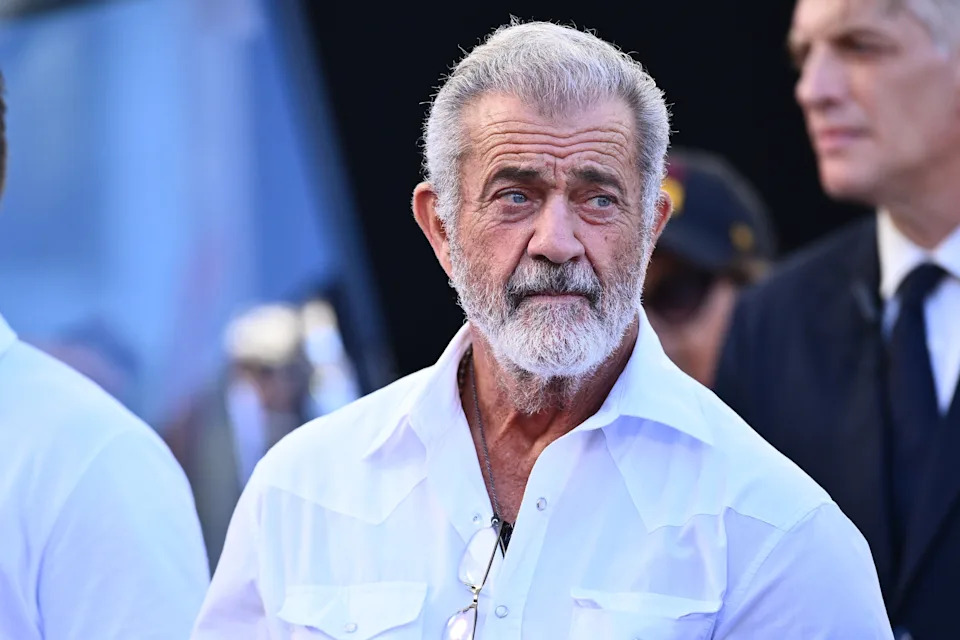 Mel Gibson in a white shirt with a beard looks sideways in a formal setting