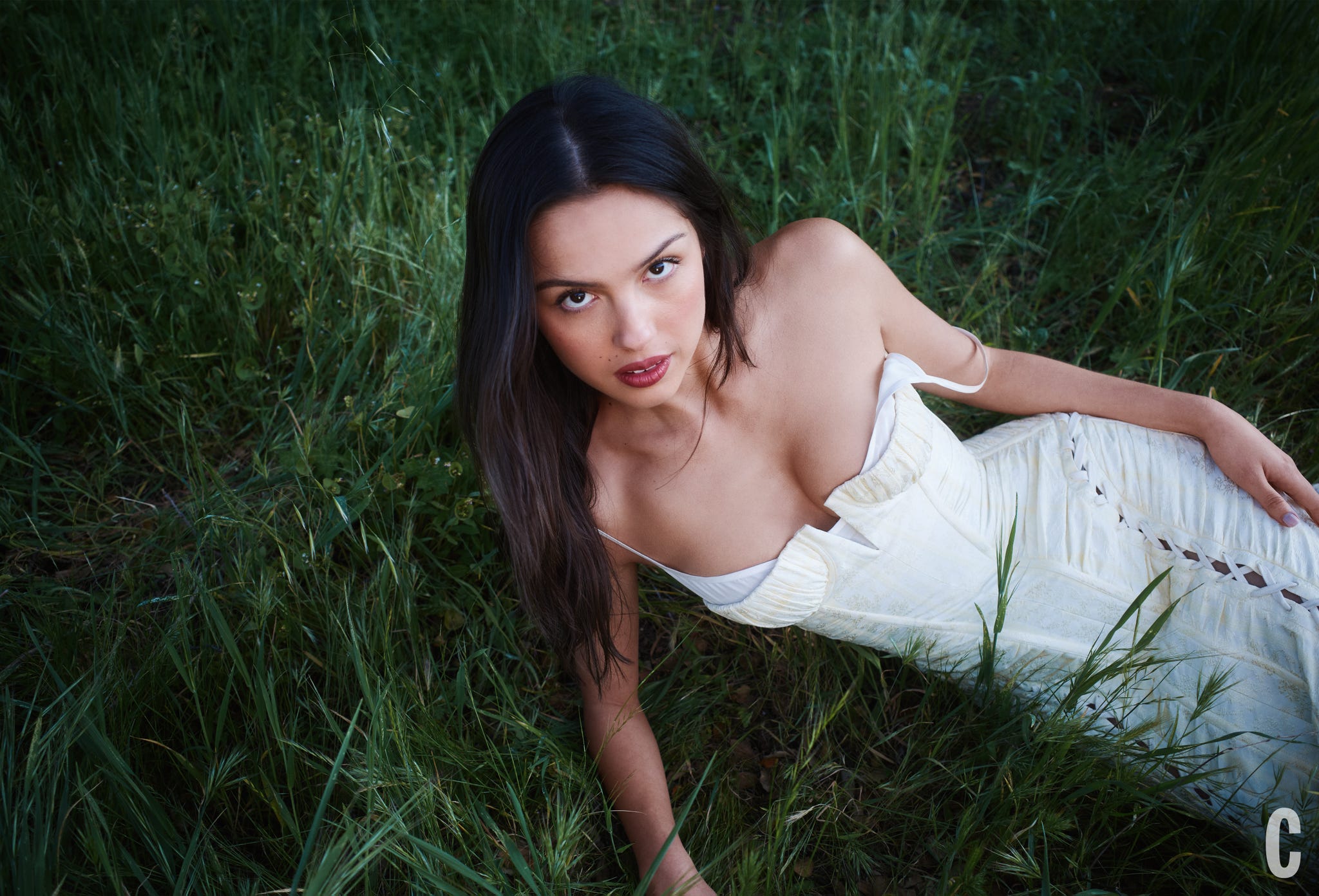 A person lying in tall green grass, wearing a white dress.