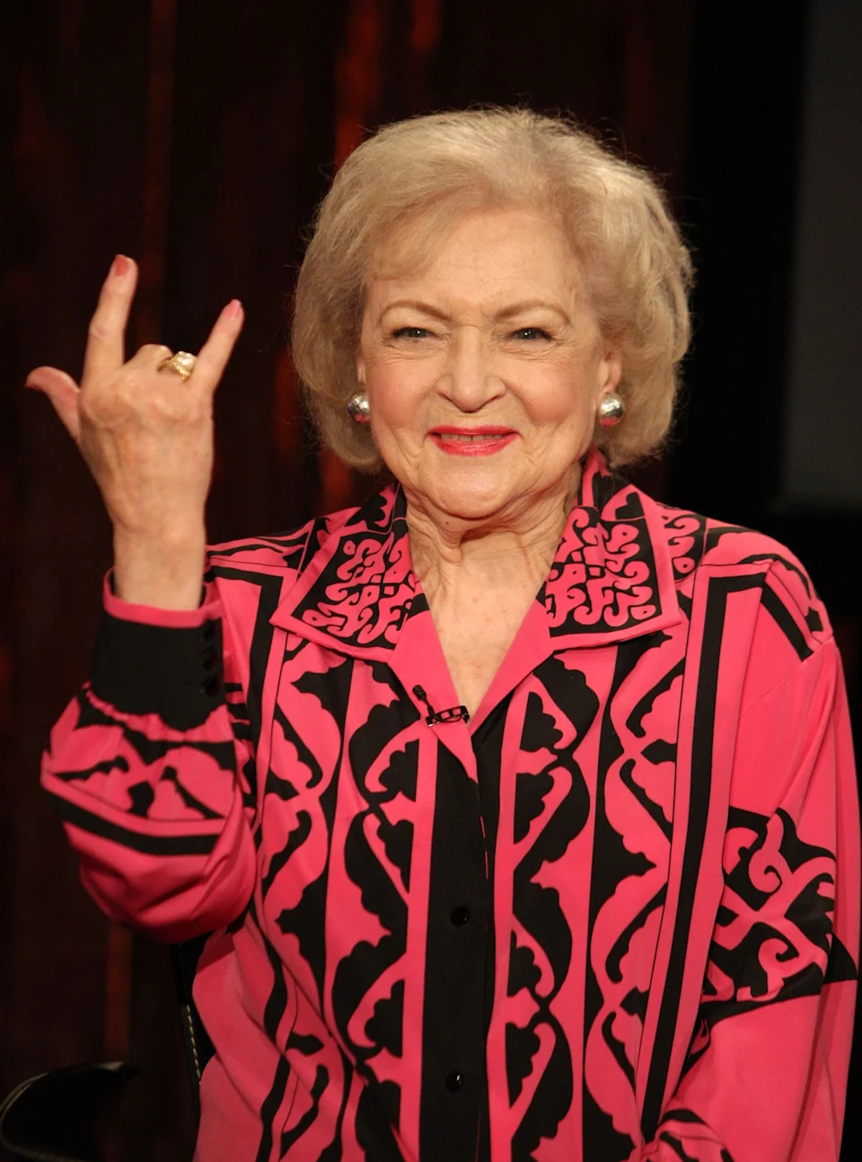 Person wearing a stylish patterned blouse, smiling and making a rock and roll hand gesture