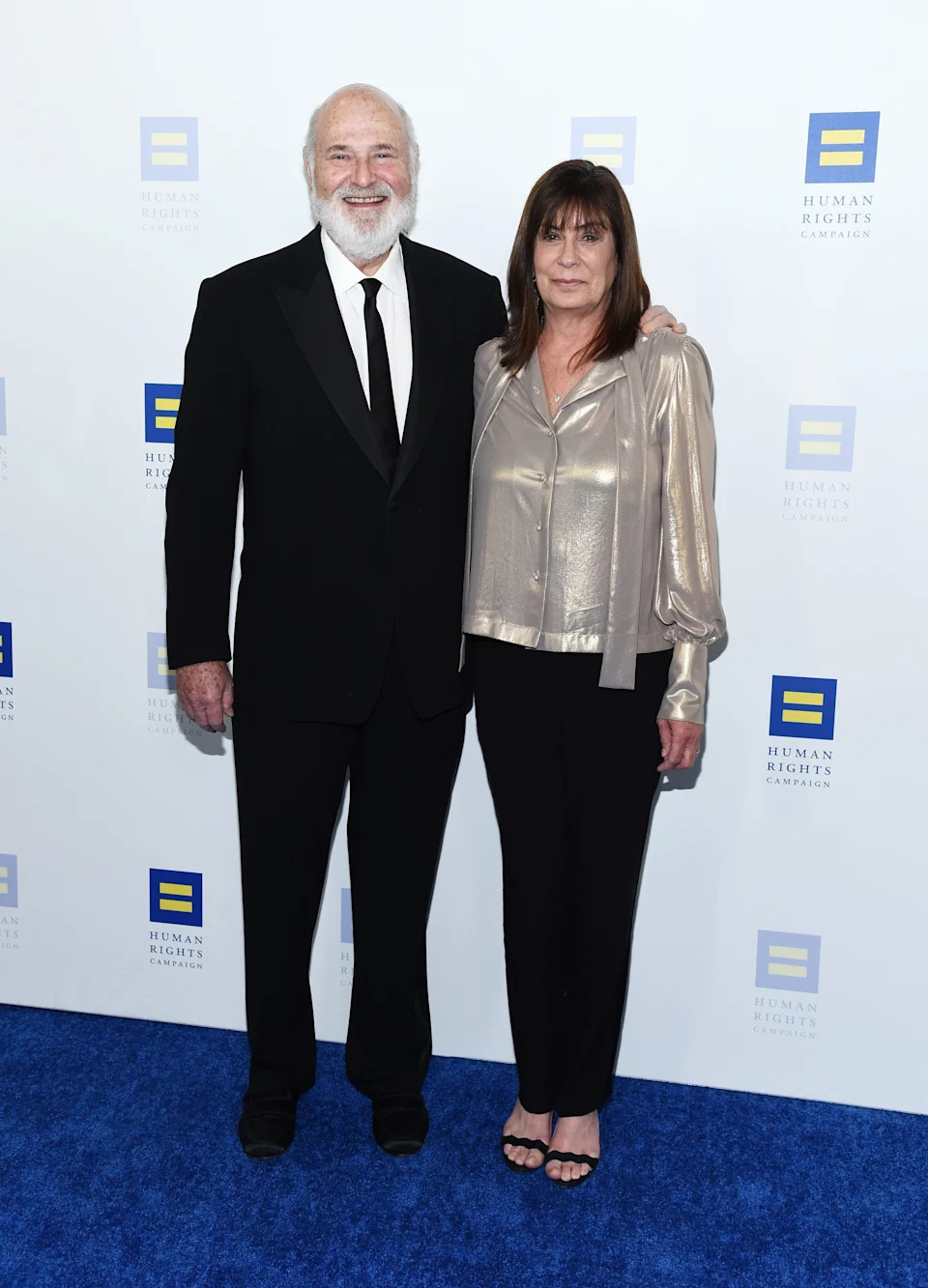 Rob and Michele Reiner pose together at an event, him in a suit and her in a metallic blouse and pants, against a Human Rights Campaign backdrop