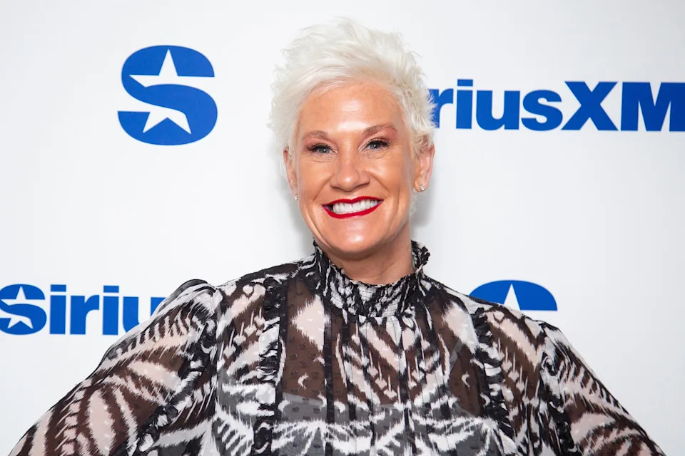 Anne Burrell smiling at a SiriusXM event, wearing a patterned high-neck dress with sheer sleeves and short hair