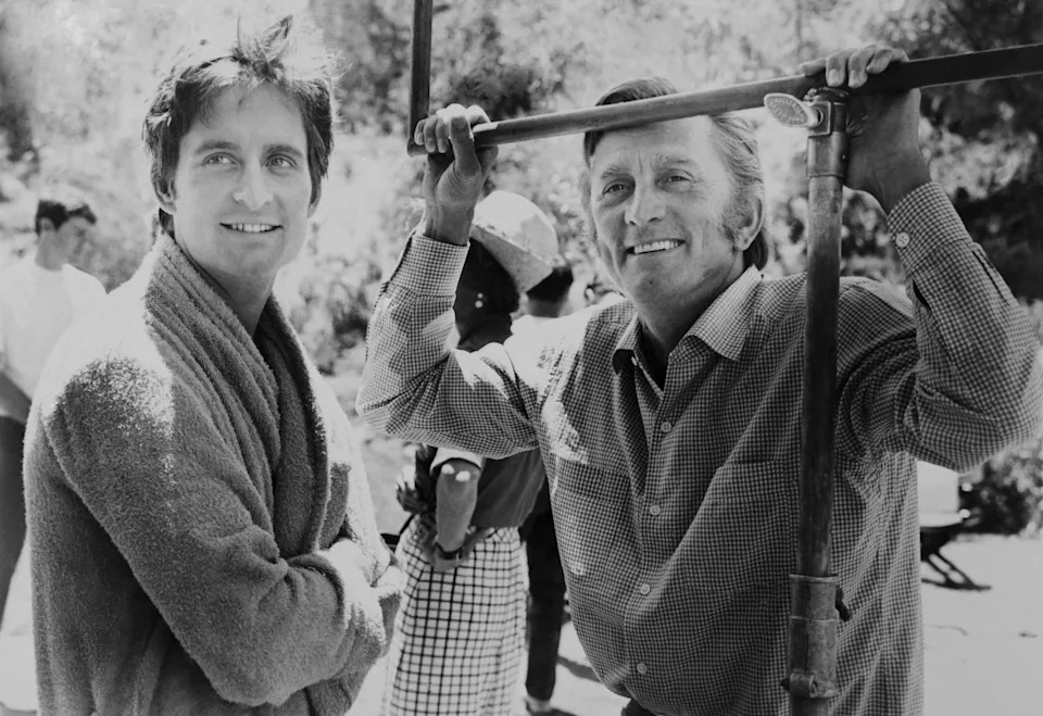 Kirk Douglas and Michale Douglas stand smiling together on a film set