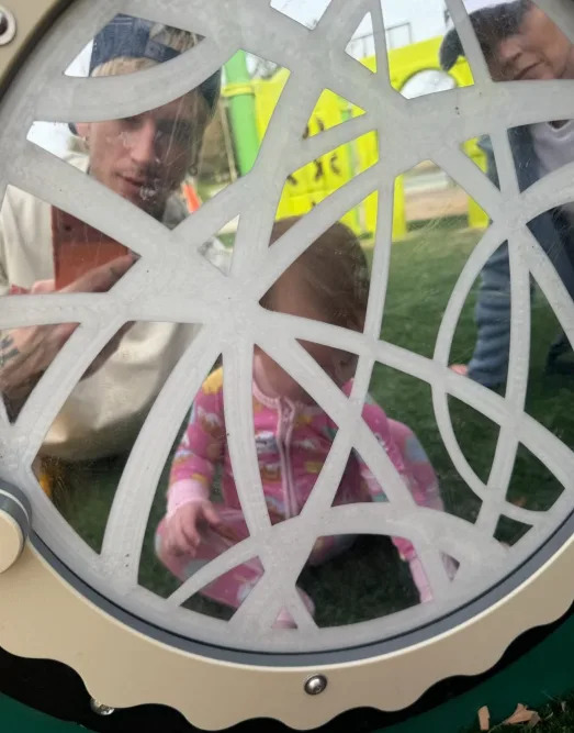 Three people, including a child, playfully gather around a playground panel with circular designs