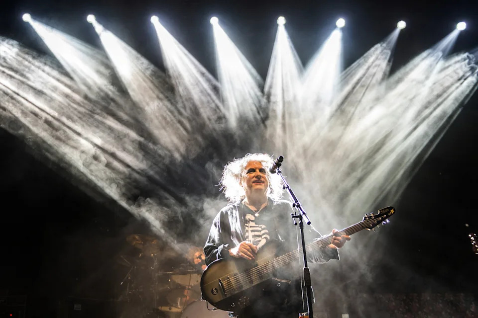 Musician performing energetically on stage with dramatic lighting and a guitar