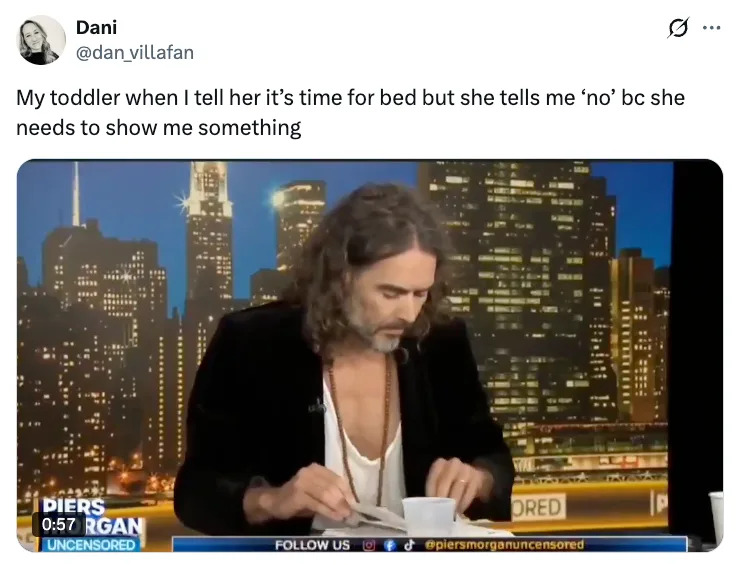 A man with long hair and an open shirt reads a paper on a TV set with a cityscape backdrop. The tweet humorously compares this to a toddler's bedtime defiance