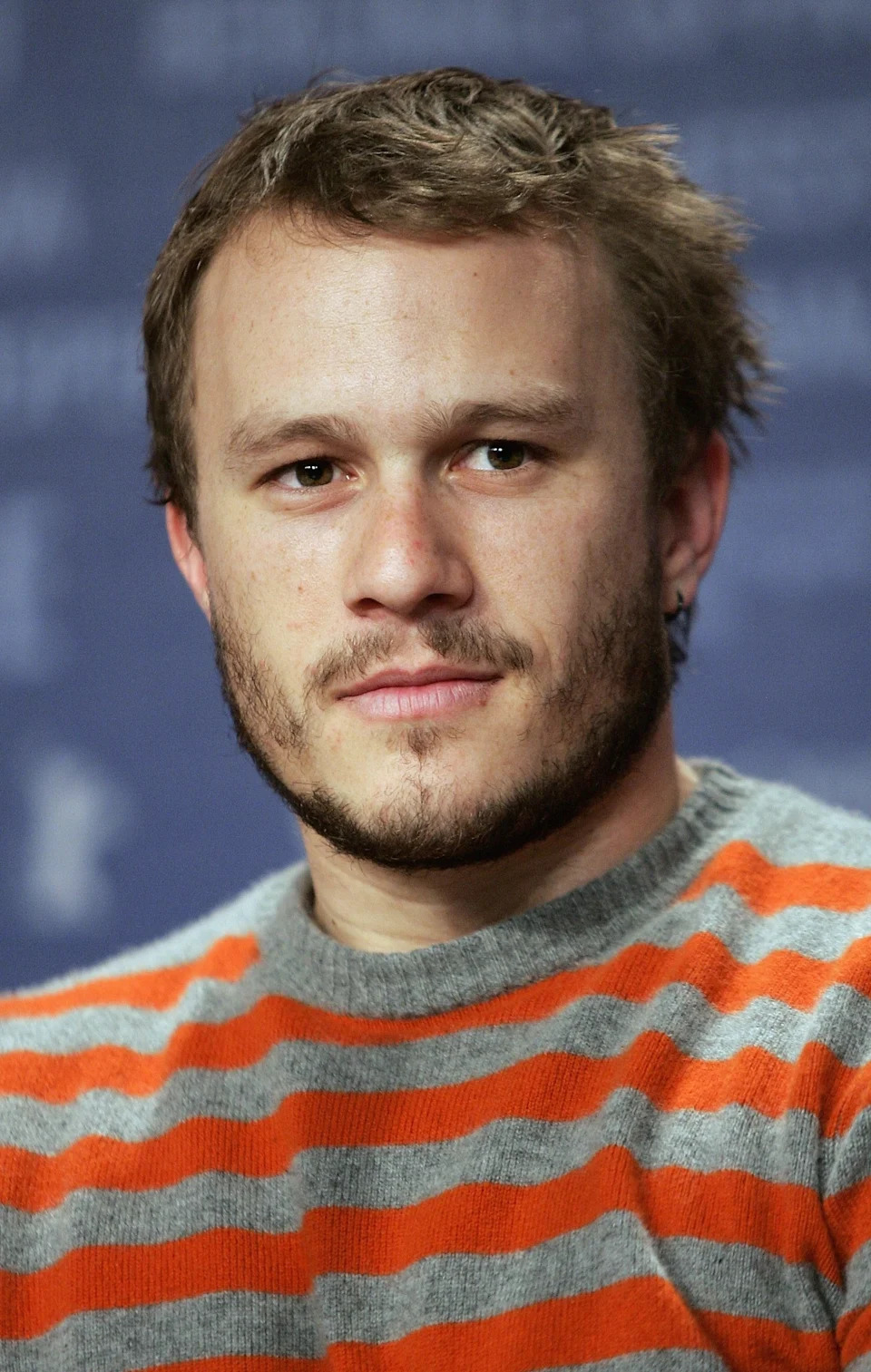 Heath Ledger with short hair and beard wearing a striped sweater