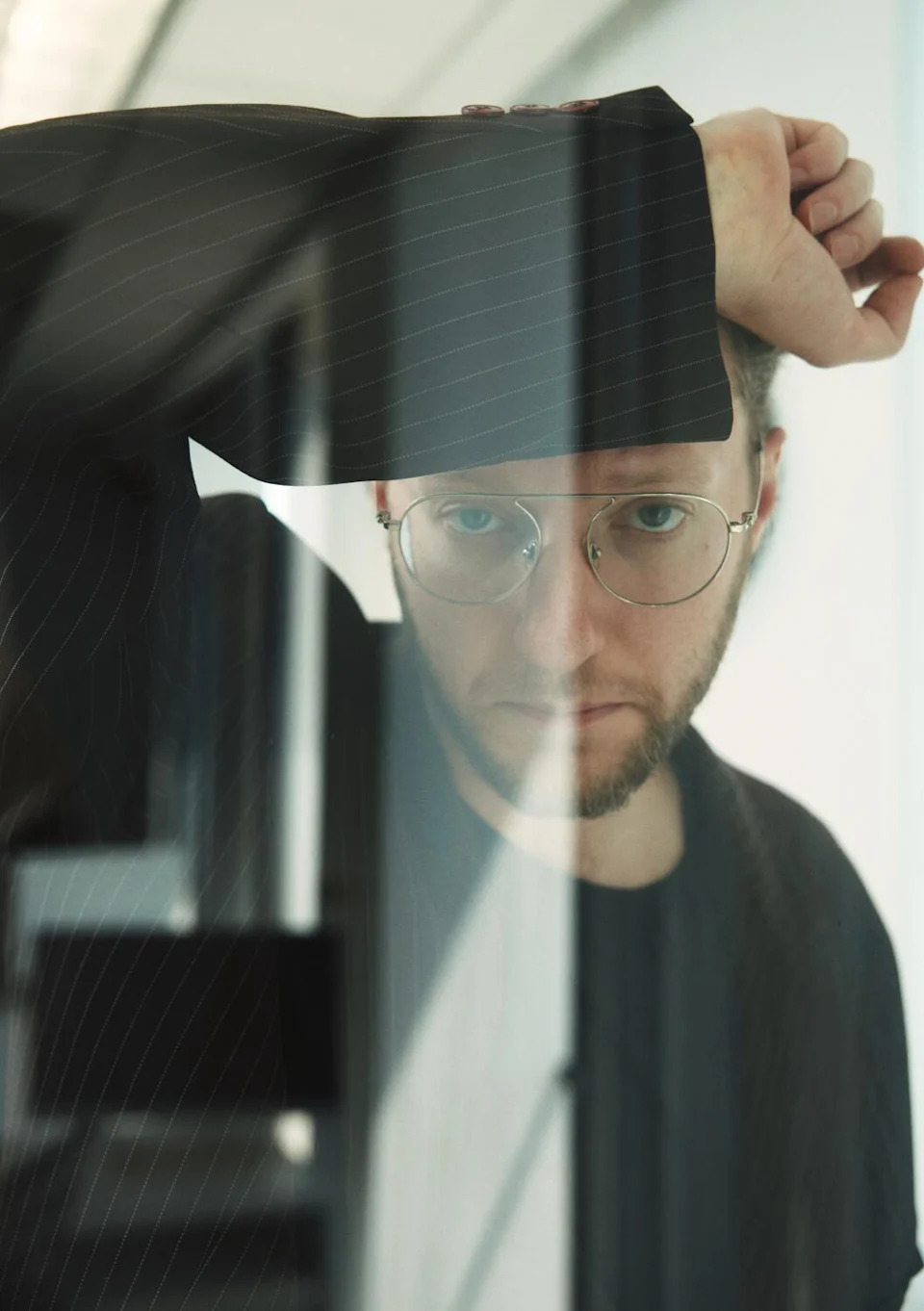 A man in a blazer puts his arm on his forehead.