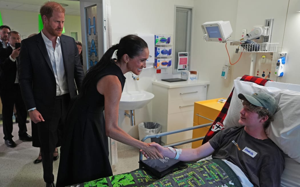 Britain's Prince Harry (L), Duke of Sussex, and his wife Meghan (C), the Duchess of Sussex, meet a patient during a visit to the Adolescent Oncology and Rehabilitation ward at the Royal Children's Hospital in Melbourne on April 14, 2026.
