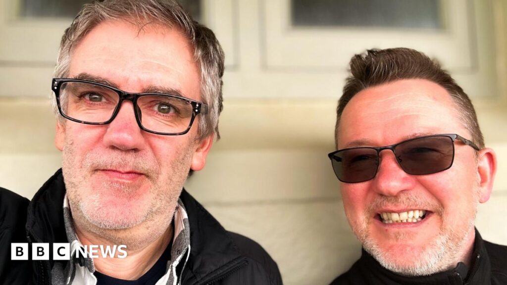 Stuart and Carl pose for a selfie. They both smile and are wearing glasses.