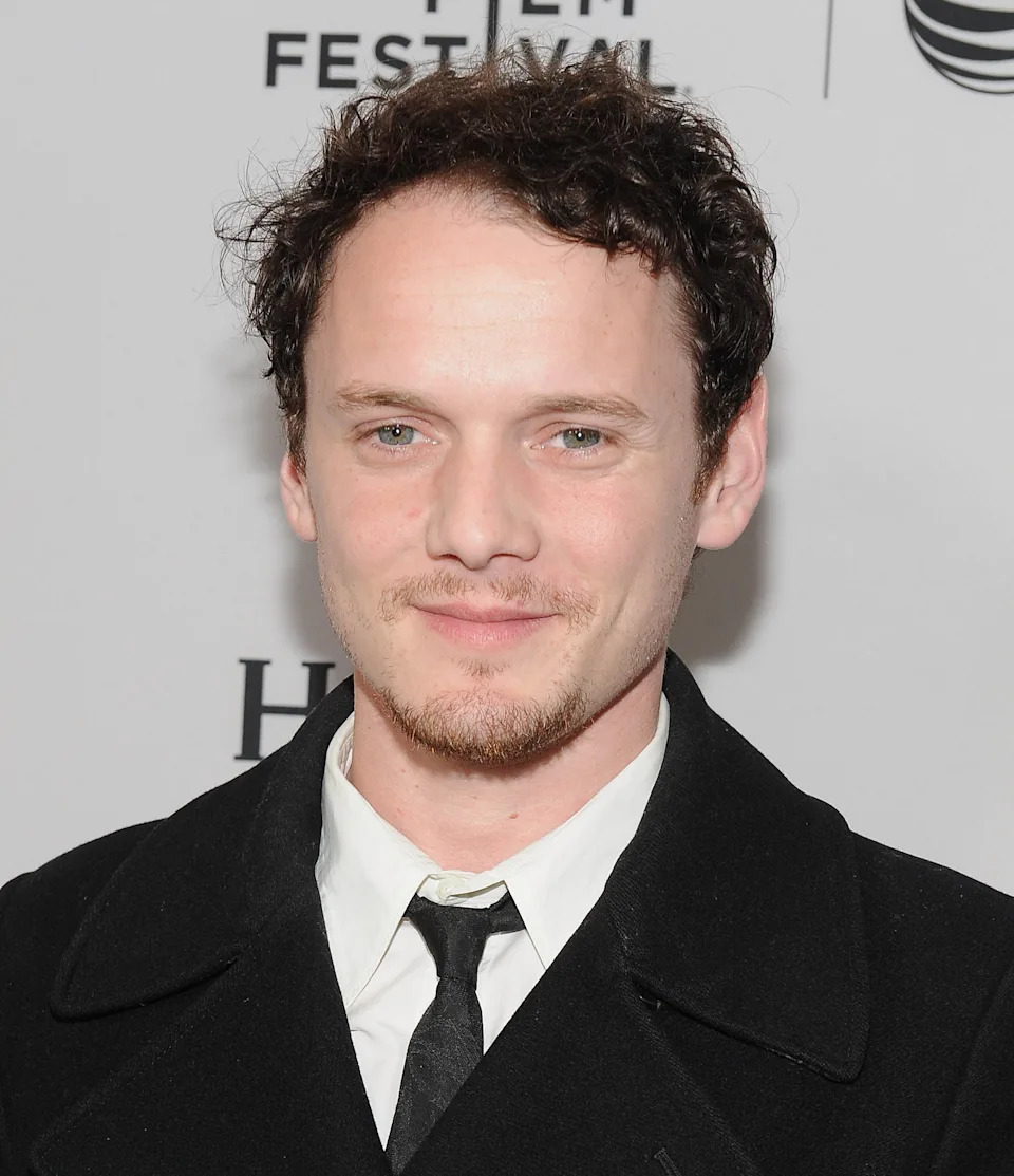 Anton Yelchin in formal attire with a tie and coat at a film festival event backdrop, smiling at the camera