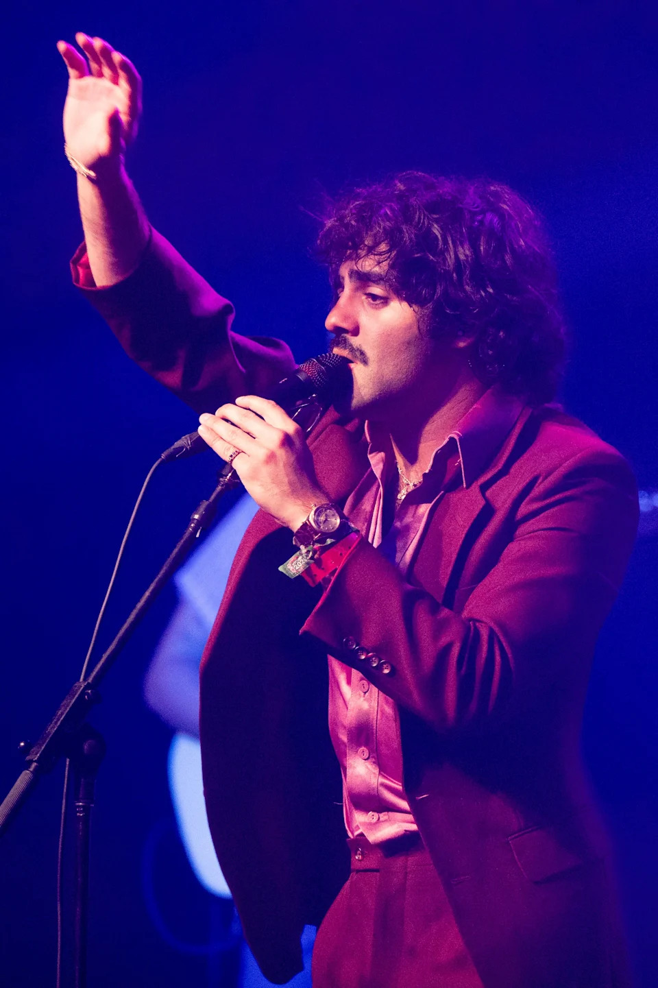 54 Ultra in a stylish suit performs passionately on stage with a microphone, raising one hand