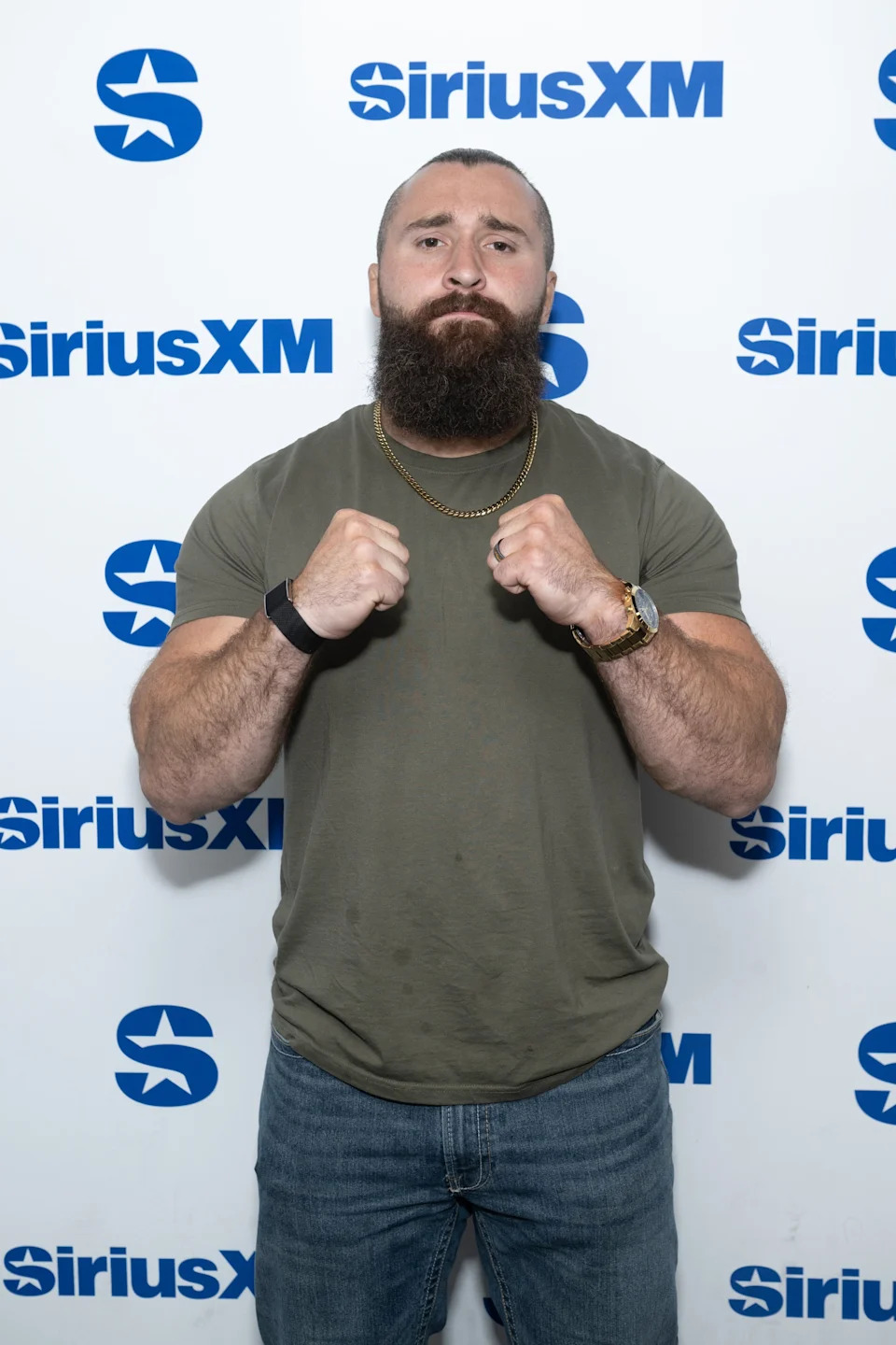 Person posing at a SiriusXM event, wearing a casual t-shirt and jeans, with a chain necklace and watch, fists playfully raised
