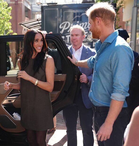 An individual in a dress and another in a blue shirt are standing near an open car door, with several people gathered around the