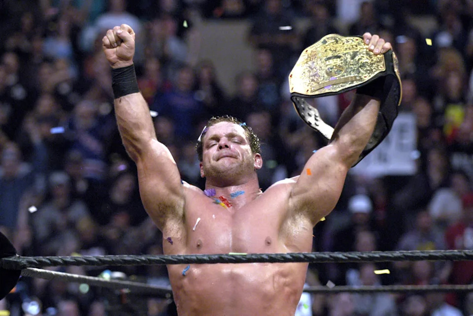Chris Benoit celebrating with championship belt in an arena, raising an arm in victory amidst confetti
