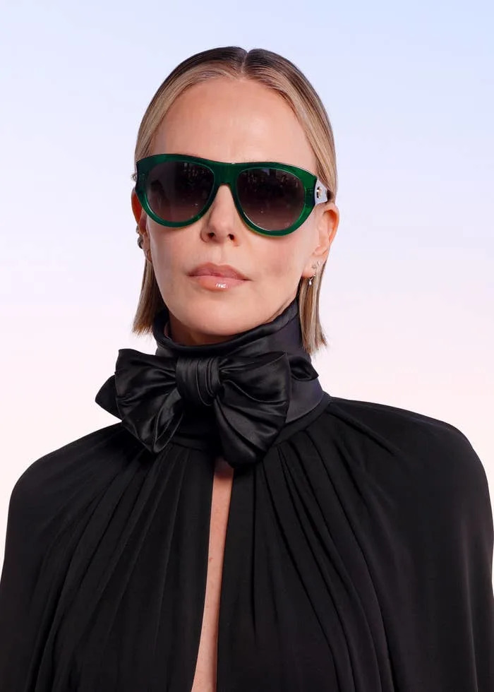 Person wearing oversized sunglasses, black high-neck gown, and large bow accessory, posing in a sleek, modern style