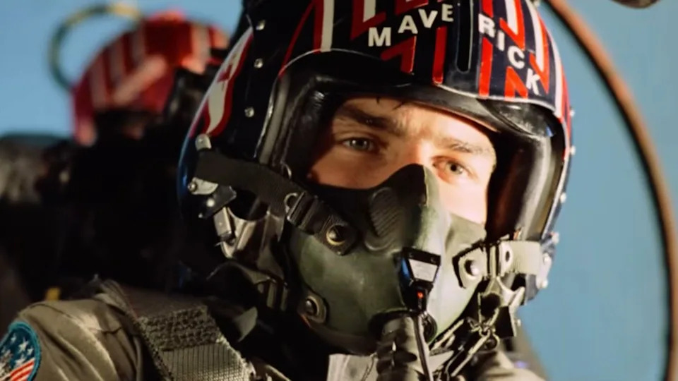  Tom Cruise as Maverick in Top Gun flying and wearing a helment that says "Maverick." . 