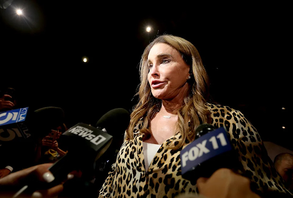 Caitlyn Jenner in a leopard print outfit speaks to reporters surrounded by microphones at a press event