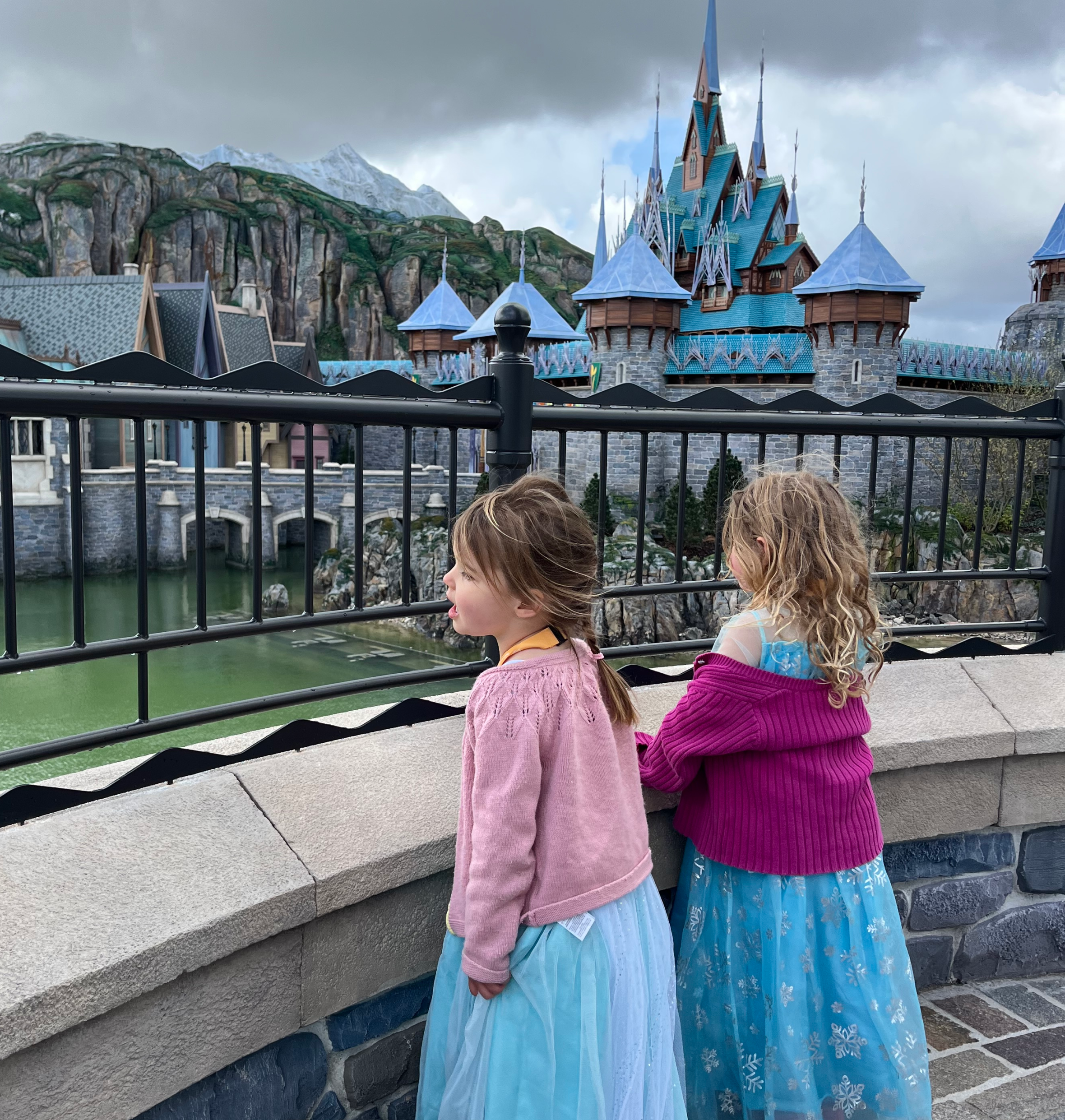 Two young girls in princess dresses look out at a Disney World of Frozen attraction.