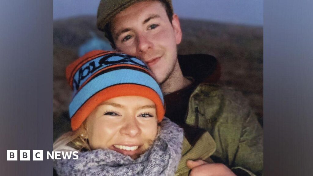 Dr Caroline Muirhead, wearing a blue and red woolly hat and a grey scarf, with Alexander 'Sandy' McKellar standing behind her, wearing a cap and dark jacket