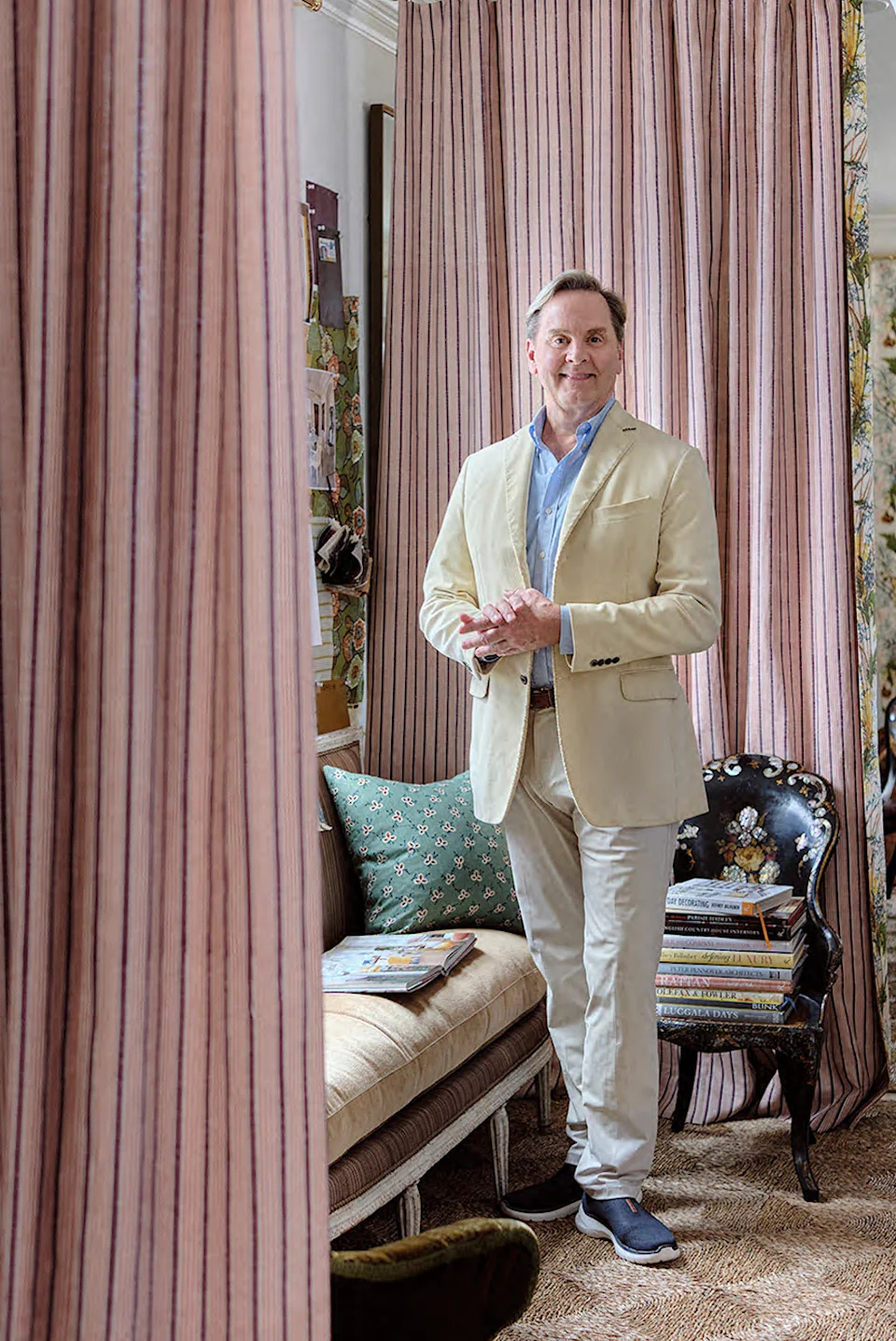 Man in a tailored outfit standing in a stylish room with curtains and decorative elements.