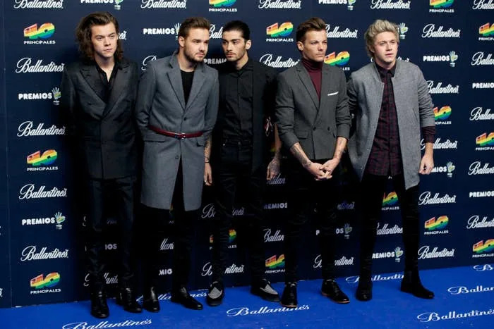 One Direction in stylish suits stands on a carpet at a celebrity event