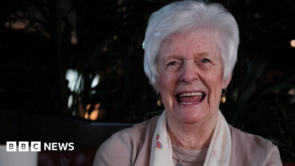 Marie McLaren smiles for the camera. She has short grey hair and is wearing a white scarf.