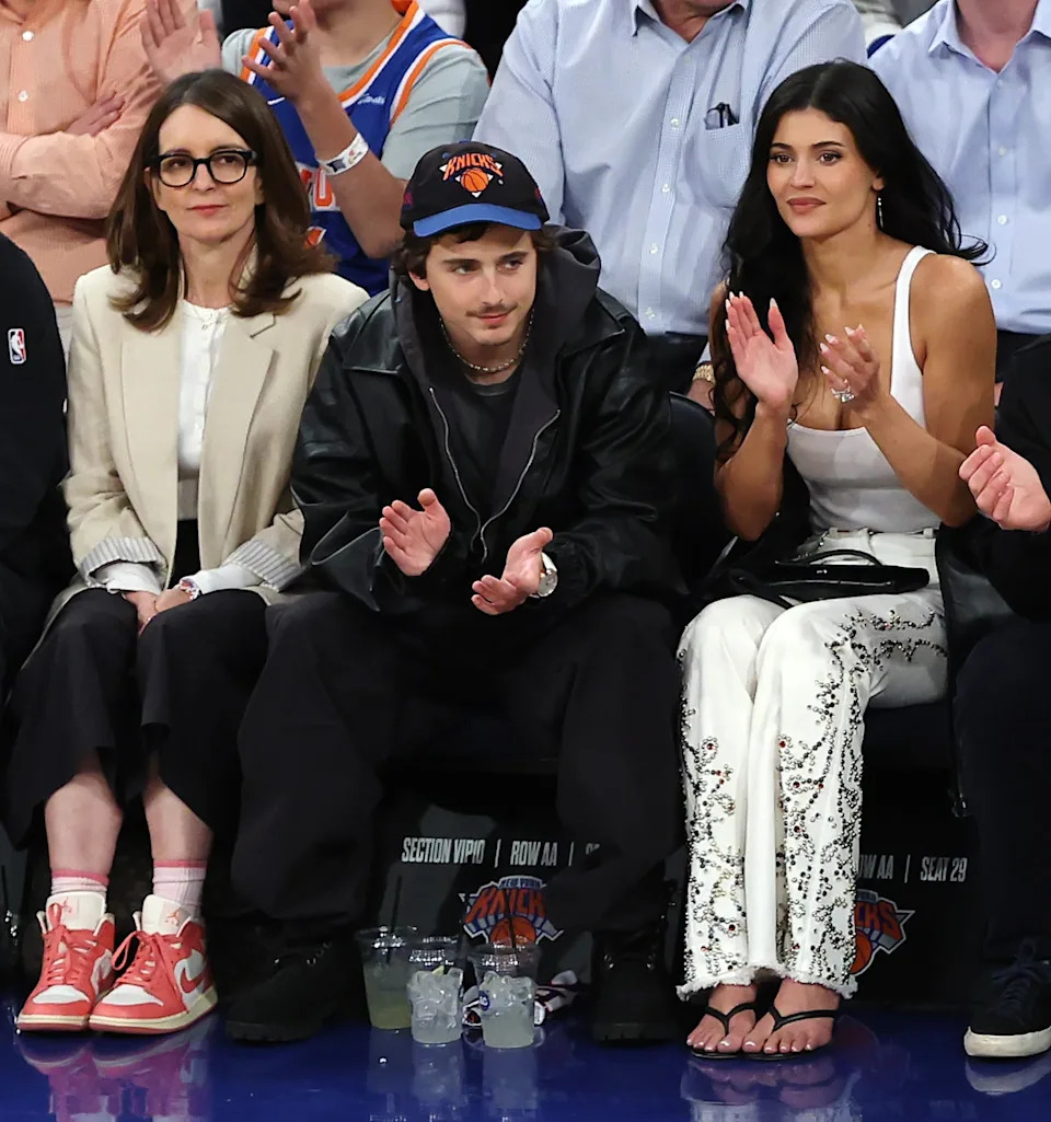People sitting courtside at a basketball game, clapping and watching the action