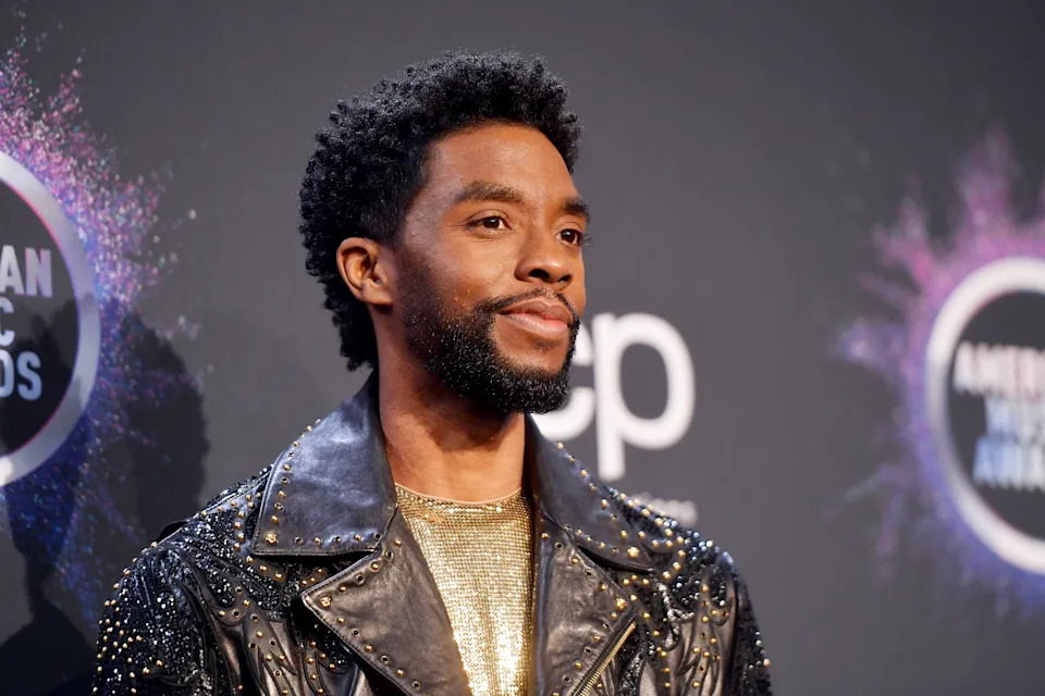 Chadwick Boseman in a studded leather jacket and shimmering top on a stage with American Music Awards logos in the background