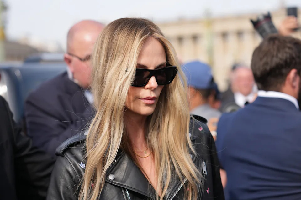 Person with long hair and sunglasses wearing a leather jacket, surrounded by a crowd outdoors