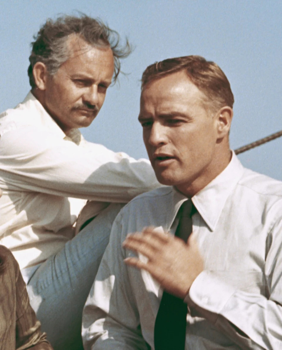 Marlon Brando and Wallyl Cox are in conversation outdoors.
