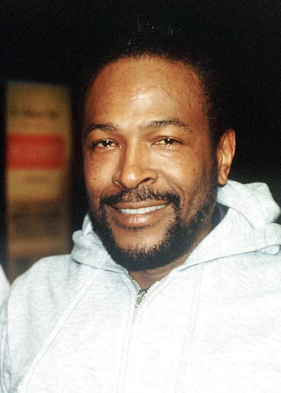 Marvin Gaye smiling, wearing a casual hoodie, in an informal setting