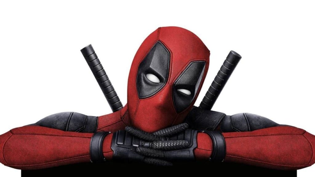 A person in a red and black Deadpool costume with a mask and two swords on their back poses with crossed arms.