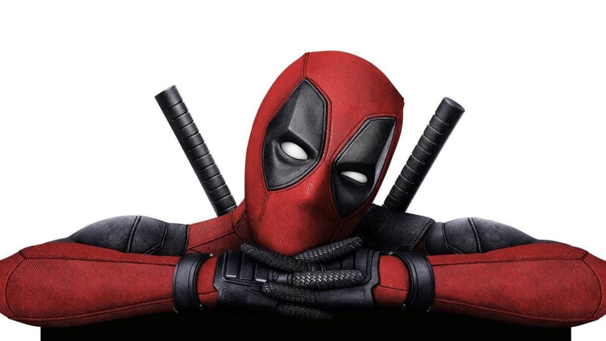 A person in a red and black Deadpool costume with a mask and two swords on their back poses with crossed arms.